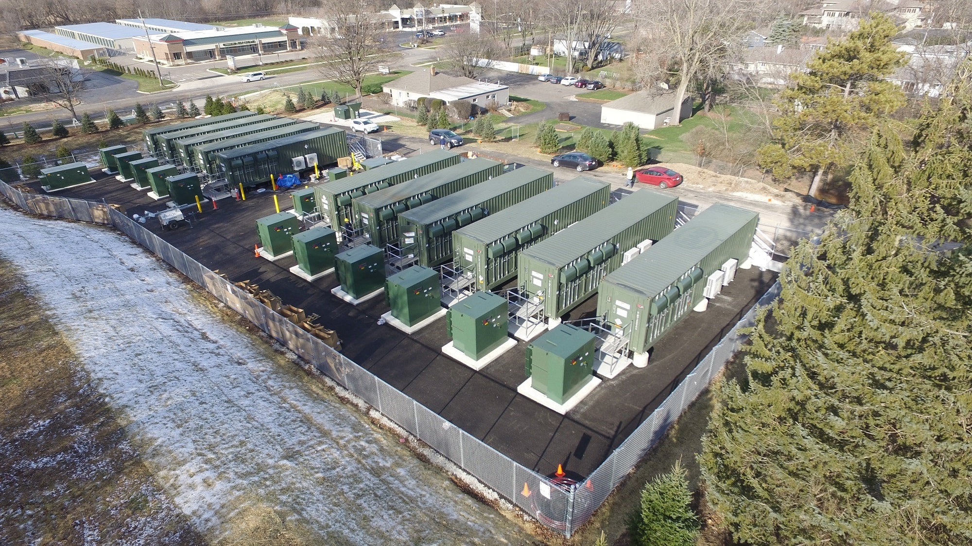 Aerial view of a battery storage yard beside a suburban corridor