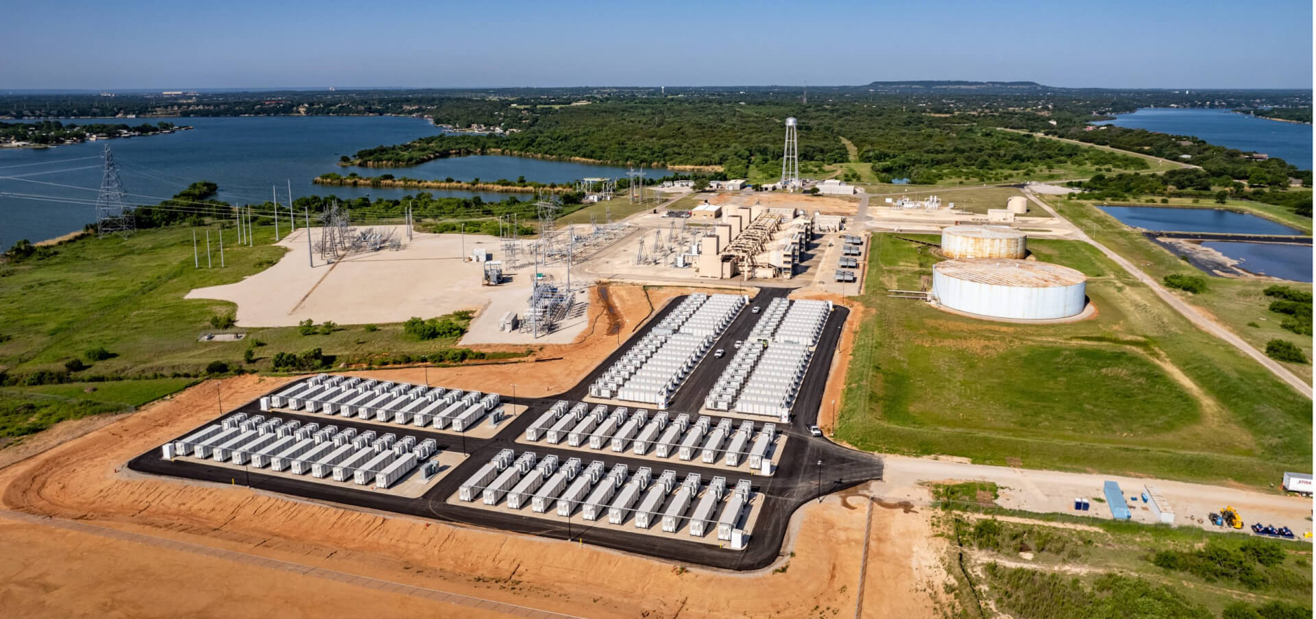 Aerial view of a utility-scale battery storage facility beside a substation and lakes
